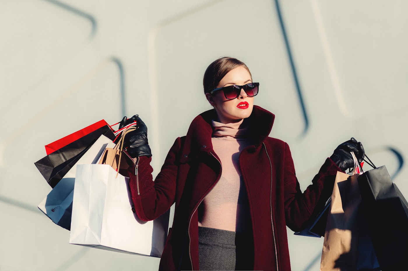 Woman wearing sunglasses and a red jacket, carrying shopping bags